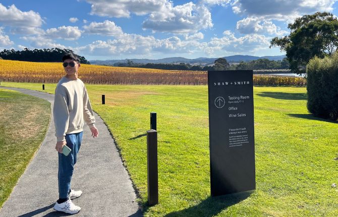 Man standing in front of blue sky, green grass and vineyards